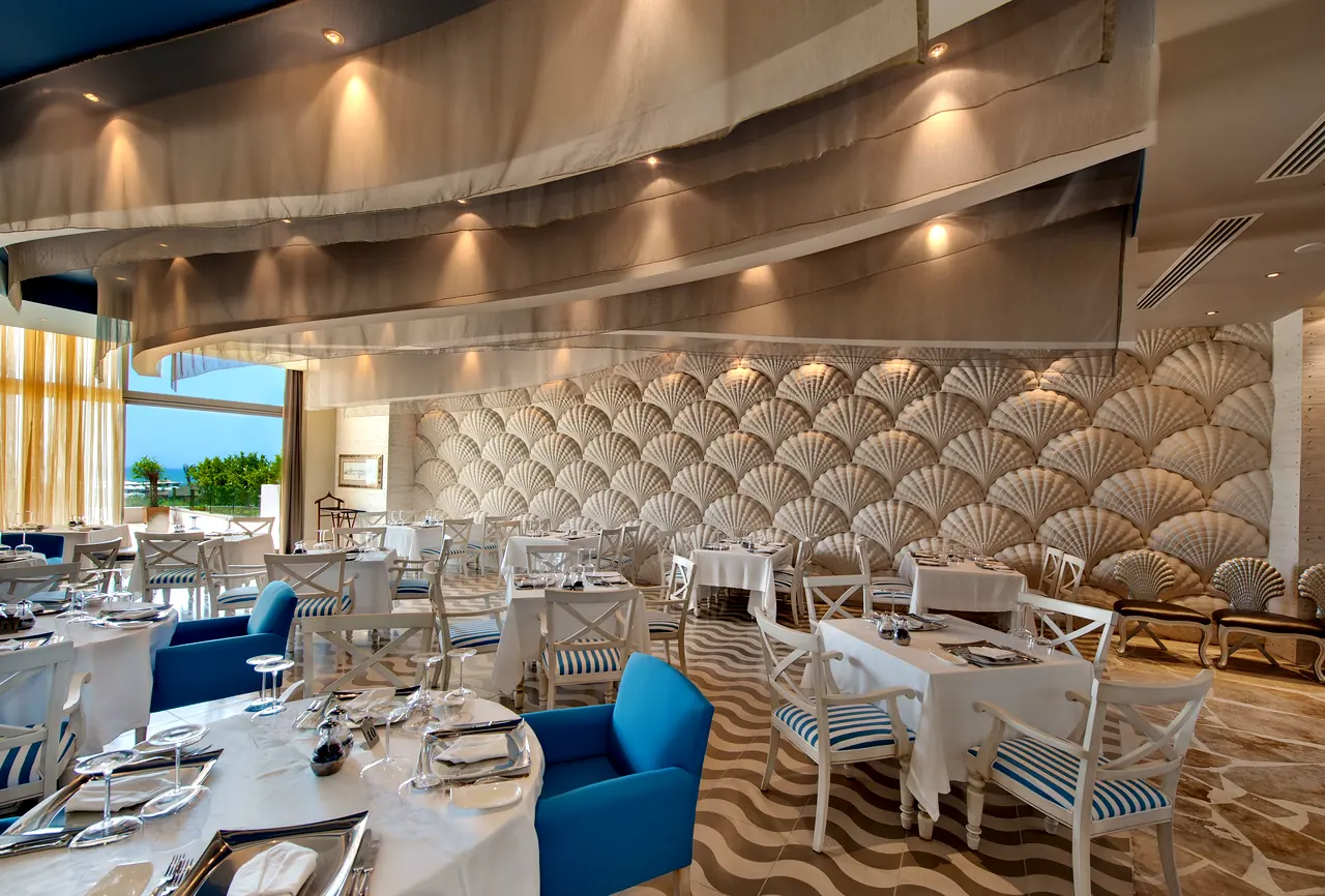 Maxx Royal Belek — Restaurant with a fan-patterned wall and blue armchairs